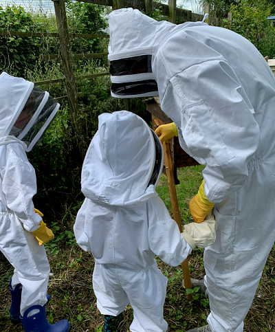 Beekeeper with two children in protective clothing looking at an apiary