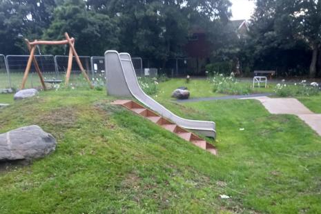 Wide-angle view of play area including basket swing, slide and wavy path