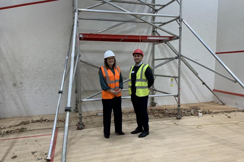 Two people standing in the former squash court with scaffolding behind
