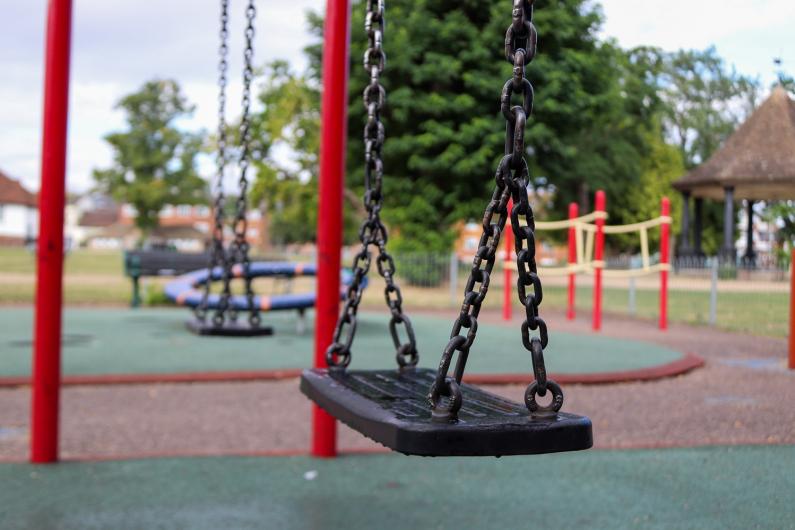A swing in the foreground with the playground in the background